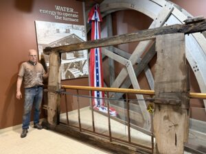 Man standing by large wooden waterwheel.